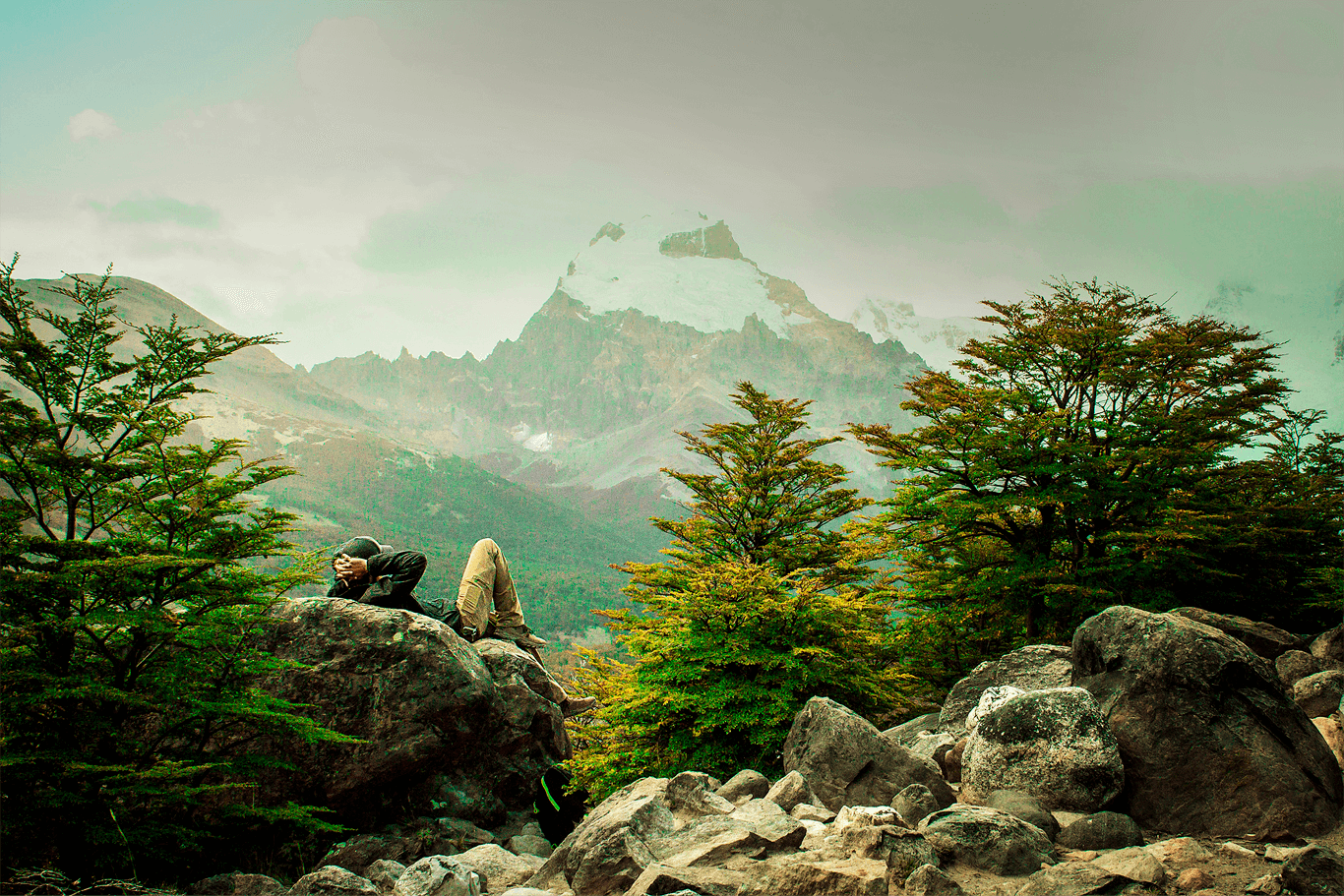 Imagem de uma pessoa deitada numa pedra, admirando a natureza com suas árvores e montanhas